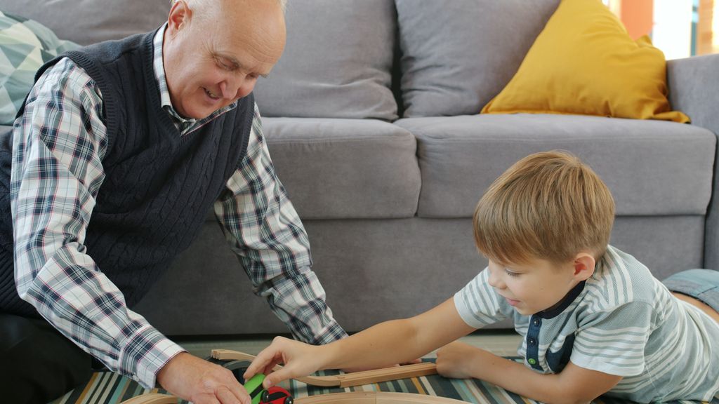 A joyful moment of grandfather playing with grandson on the floor with a toy train.
